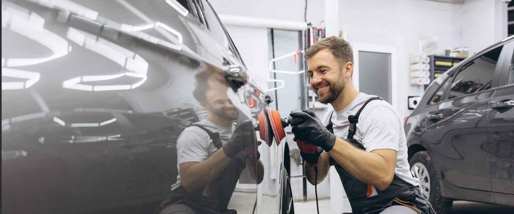 Selbstständig als Fahrzeugaufbereiter - Fahrzeugaufbereiter poliert ein Auto in seiner Halle und lacht dabei