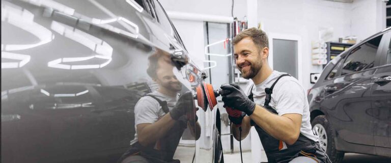 Selbstständig als Fahrzeugaufbereiter - Fahrzeugaufbereiter poliert ein Auto in seiner Halle und lacht dabei